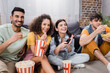 © LIGHTFIELD STUDIOS - laughing woman holding remote controller near friends eating snacks while watching tv