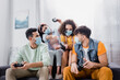 © LIGHTFIELD STUDIOS - Hispanic friends in medical masks holding joysticks on couch