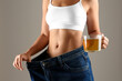 © New Africa - Young woman in old big jeans with cup of tea showing her diet results on beige background, closeup