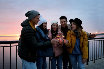 Canvas Print - People in warm clothes holding burning sparklers near river