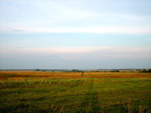 A Flat Horizon Line Between The Sky And The Earth. The Sky And Clear Field In The Countryside Are Illuminated By The Rays Of The Setting Sun.