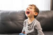 © Louis-Paul Photo - Little boy is standing on sofa at home with a big laugh