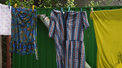 Wet colorful laundry hanging on clothesline rope outdoor. Traditional way to dry clothes on clothespins in village courtyard against background of green fence. Authentic rural life scene