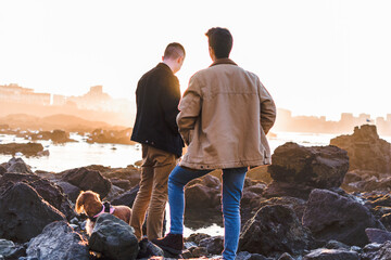 Two young men and a dog (Cocker Spaniel) looking at the horizon on beach rocks