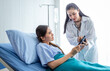 © Thinapob - Asian female doctor therapeutic advising with tablet to young female patient on Bed in hospital background.