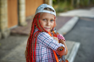 Portrait of a little girl in dreadlocks with a skate on the street . The concept of youth culture