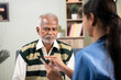 © WESTOCK - Shoulder shot of doctor explaining to patient about health details by using mobile app on phone during routine home visit
