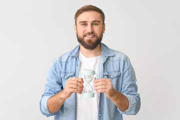 Canvas Print - Young man with hourglass on light background