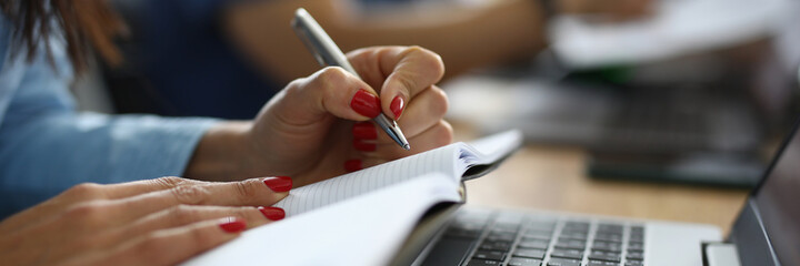 Wall Mural - Female hands hold pen and diary next to laptop at work table. Training profession copywriter online concept