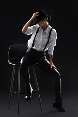 Wall Mural - Beautiful fashionable young woman sitting on chair against dark background