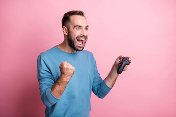 Photo of excited lucky guy wear blue pullover playing playstation looking empty space rising fist isolated pink color background