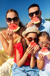 © Syda Productions - family, leisure and people concept - happy mother, father and two daughters having picnic on summer beach and eating watermelon
