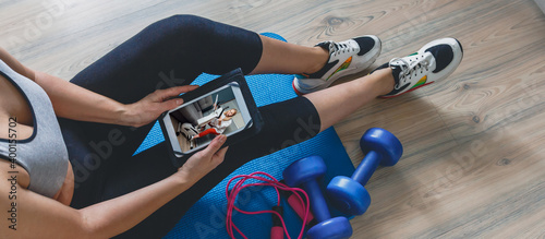Fitness at home, remote training with virtual instructor. Woman in sportswear sitting on the floor with dumbbells laptop at home. Sports and recreation concept in lockdown with fitness apps online