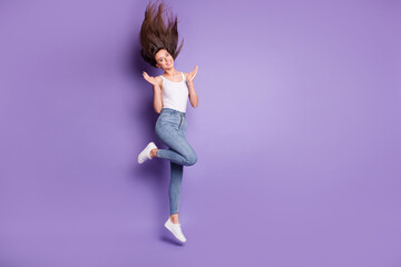 Poster - Full size photo of slim happy brown haired woman jump up wear jeans raise palms isolated on purple color background