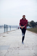 Wall Mural - Athletic sporty man training in hoodie sweatshirt in urban city park near the river.