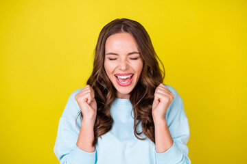 Wall Mural - Photo of cute funny young girl raise fists open mouth eyes closed delighted screaming yeah win big bet horse racing wear blue pullover isolated vibrant yellow color background