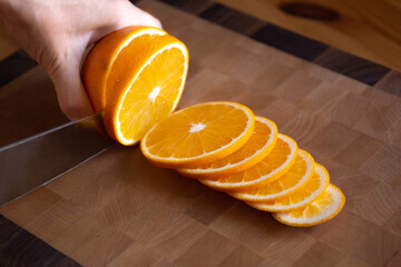 Chef's knife in hand cuts an orange into slices on a cutting board