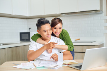 Happy young couple husband and wife using laptop computer looking at screen pay bills online in app calculate mortgage investment payment