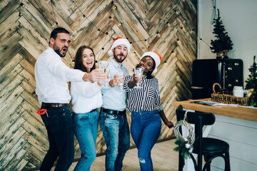 Wall Mural - Joyful multiethnic adult friends with glasses cheering at Christmas party