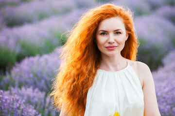 Summer portrait of a beautiful girl with long curly red hair. European girl in lavender field. Wavy Red Hair