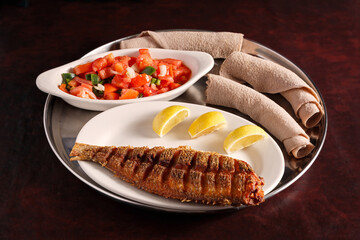 Ethiopian platter of grilled fish, injera bread and salad on a dark wooden surface