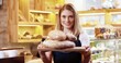 © VAKSMANV - Close up portrait of happy beautiful young Caucasian woman seller bakery owner in apron standing in small store and holding tray with fresh baked bread in hands, smelling baking and smiling to camera