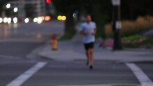 Man Running Across Crosswalk Coming Into Focus As He Exercises In The City At Dusk.