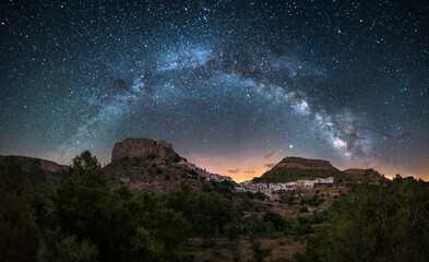Wall Mural - Night panoramic view of the Milky Way over a town in Spain, Chulilla. Night landscape of a village between mountains illuminated by the stars of the Milky Way. Chulilla, a town in Valencia, Spain