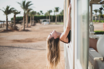 Wall Mural - cute young teenage girl or woman posing and having fun on the beach cafe window under palm trees in summer swimsuit . Trendy girl posing. Funny and positive woman.