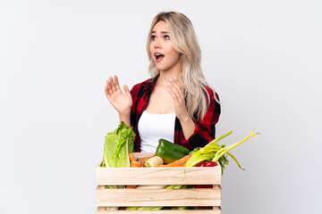 Farmer girl holding a basket full of fresh vegetables over isolated white background with surprise facial expression