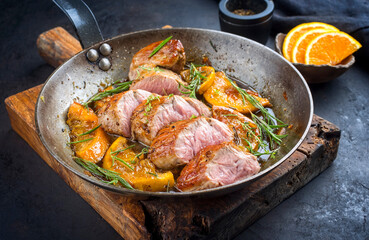 Wall Mural - Traditional fried pork filet medaillons in with caramelized orange slices and herbs served as close-up in a rustic wrought iron skillet