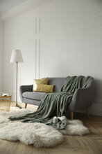 Stylish Room Interior With Comfortable Sofa, Knitted Blanket And Lamp Near White Wall