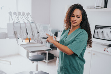 Wall Mural - Young blond Caucasian female opening her mouth while African-American ethnic dentist in white latex gloves check condition of her teeth (focus on dentist)