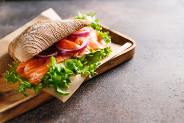 Wall Mural - Healthy sandwich with rye bread bun, salmon, avocado, onion and salad served on a wooden rustic board.