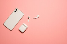 Top View Layout On An Isolated Pastel Pink Background With Wireless Earphones With A Case, And A Modern White-colored Mobile Phone.