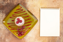 Overhead View Of Mini Cake With Fruits On A Green Plate And Notebook On Mixed Color Background