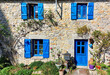 Façade d'une maison en pierre de granit, avec fenêtres et volets bleus type breton, rosiers et pots colorés. Bretagne, pays bigouden