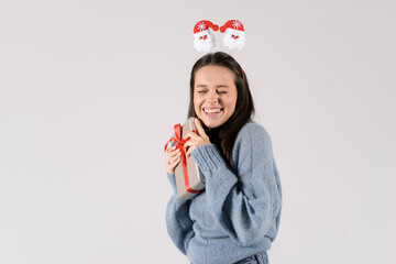 Cheerful young woman with christmas gift box happy and excited wearing funny head hoop isolated on white background