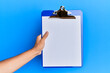 © Krakenimages.com - Young hispanic hand holding clipboard over isolated blue background.