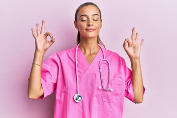 Young hispanic woman wearing doctor uniform and stethoscope relax and smiling with eyes closed doing meditation gesture with fingers. yoga concept.