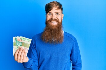 Sticker - Young irish redhead man holding hong kong 50 dollars banknotes looking positive and happy standing and smiling with a confident smile showing teeth