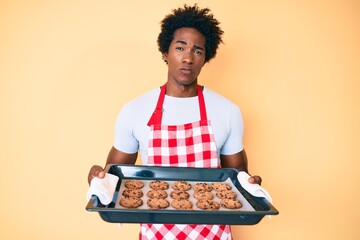 Sticker - Handsome african american man with afro hair wearing baker uniform holding homemade cookies skeptic and nervous, frowning upset because of problem. negative person.