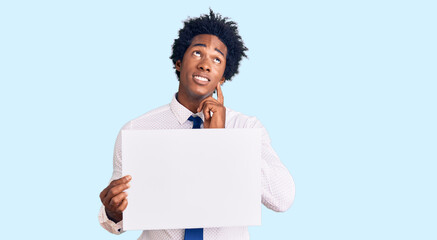 Poster - Handsome african american man with afro hair holding blank empty banner serious face thinking about question with hand on chin, thoughtful about confusing idea