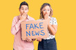 © Krakenimages.com - Couple of women holding fake news banner covering mouth with hand, shocked and afraid for mistake. surprised expression