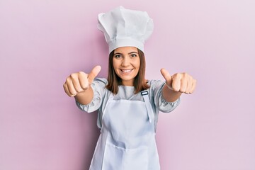 Poster - Young beautiful woman wearing professional cook uniform and hat approving doing positive gesture with hand, thumbs up smiling and happy for success. winner gesture.