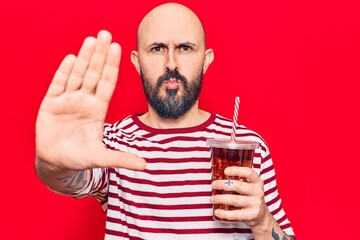 Sticker - Young handsome man drinking glass of cola beverage with open hand doing stop sign with serious and confident expression, defense gesture