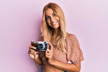 Canvas Print - Beautiful blonde young woman holding vintage camera smiling with a happy and cool smile on face. showing teeth.