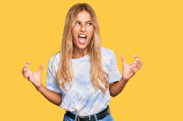 Canvas Print - Beautiful blonde young woman wearing casual tie dye shirt crazy and mad shouting and yelling with aggressive expression and arms raised. frustration concept.