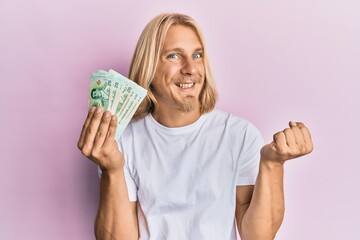 Sticker - Caucasian young man with long hair holding 20 thai baht banknotes screaming proud, celebrating victory and success very excited with raised arm