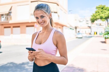 Wall Mural - Young blonde sporty girl smiling happy using smartphone at street of city.